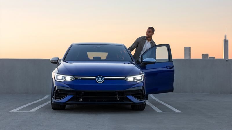 A man is getting in the 2023 blue Volkswagen Golf R parked on the parking lot.