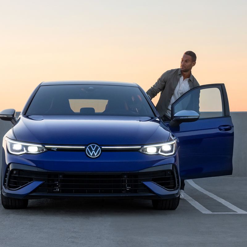 A man is getting in the 2023 blue Volkswagen Golf R parked on the parking lot.