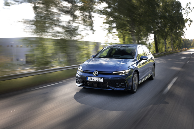 En blå VW Golf GTE kör längs en väg, gröna träd i bakgrunden