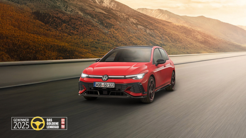 Ein roter VW Golf GTI EDITION 50 fährt im Sonnenaufgang auf einer Straße durch die Landschaft. Ebenfalls abgebildet ist das Logo des Goldenen Lenkrads 2025.
