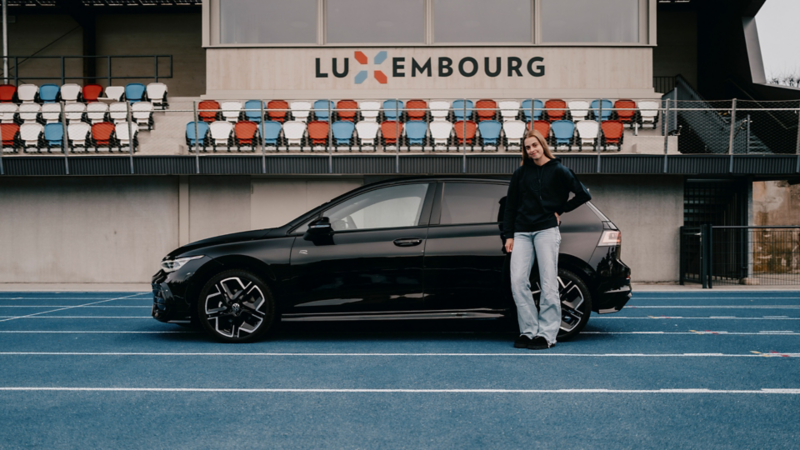 Une jeune femme se tient devant la Golf noire.