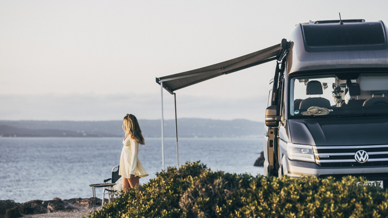 Photo showing a Grand California with the awning deployed next to a coastal background. 