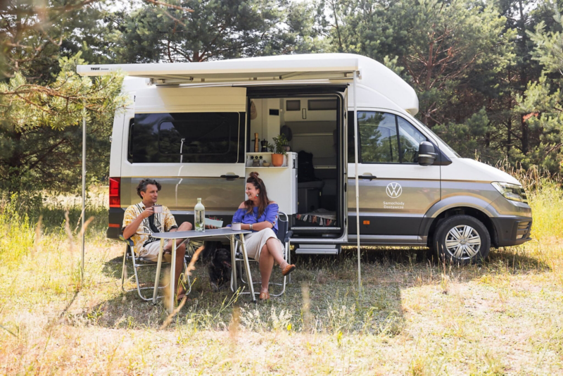 Kobieta i mężczyzna siedzą przy stoliku pod markizą Volkswagena Grand California.