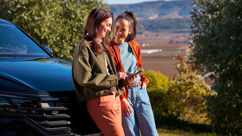 Due ragazze parlano e consultano lo smartphone appoggiate di fronte a VW Tourareg