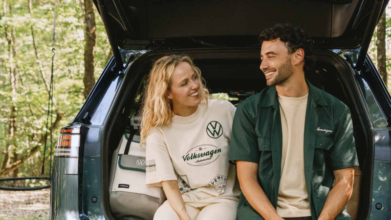 Una pareja sentada en la parte trasera de un Volkswagen rodeada de un bosque.