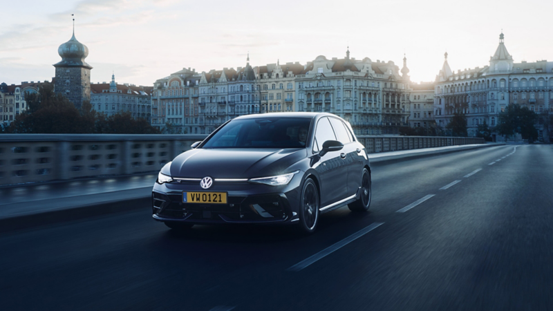 Une Golf R sombre traverse un pont dans une ville.