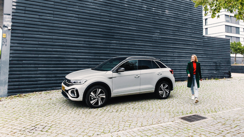 Une Tiguan rouge est garée devant un bâtiment moderne. Une femme et un garçon avec des bagages s'apprêtent à monter dans la voiture.