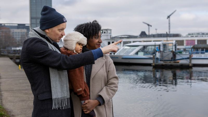 Jeniffer Mulinde Schmid steht mit ihrem Mann und ihrem Kind am Fluss und schaut auf die andere Seite