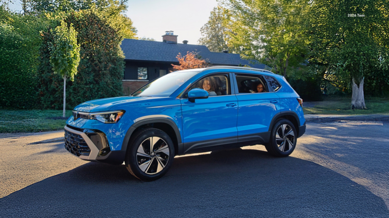 A Volkswagen Taos with two a mother and daughter is on a paved street. The scene is a sunny residential neighborhood with green trees, bushes, and a house in the background, and long shadows are cast across the road.
