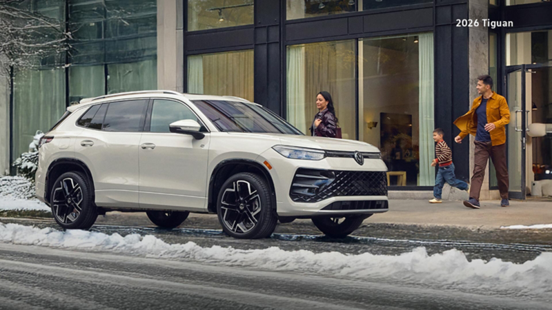 A man, woman, and child walking out of a building and towards a white Tiguan that’s parked on a snowy street.
