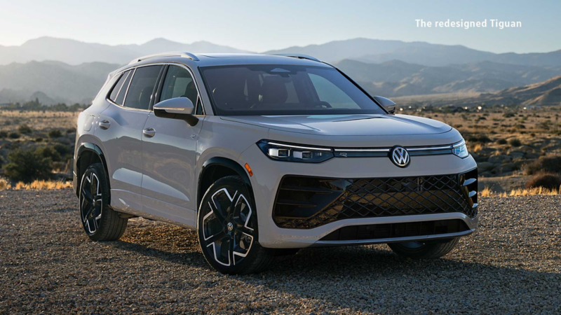 A Pyrite Silver Metallic Volkswagen Tiguan Highline R-Line in a desert landscape, with rocky hills and sparse vegetation in the background under a clear, deep blue sky.