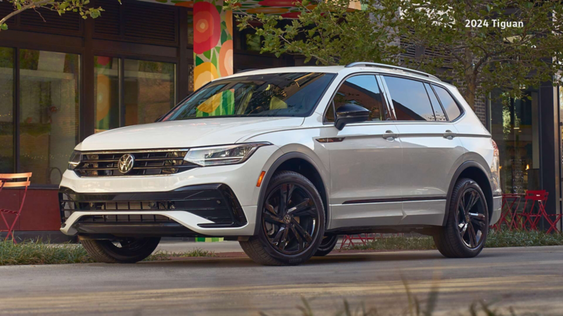 An Oryx White Pearl Volkswagen Tiguan Comfortline R-Line Black Edition parked in front of a modern building with large windows and vibrant floral decor.