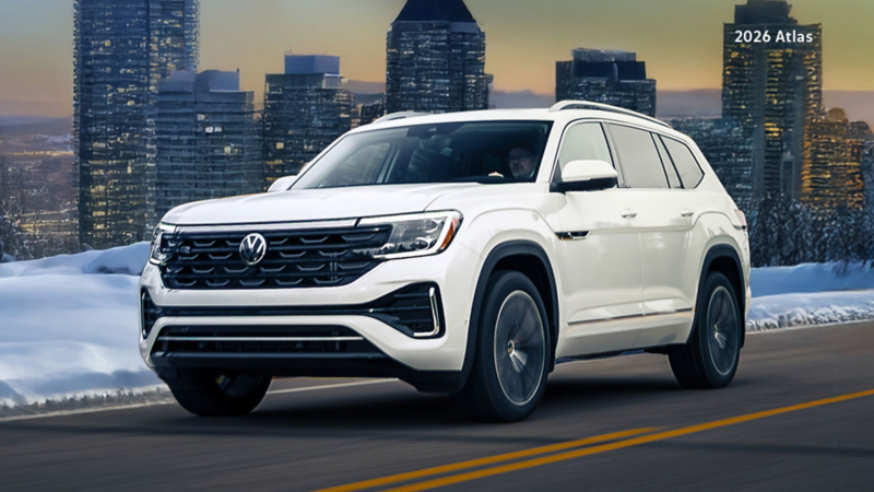 A white Atlas is driving on a road alongside a snowy hill during sunset. There is a cityscape in the background.