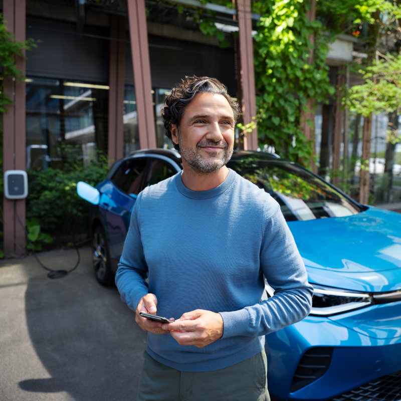 Een man lacht met zijn telefoon in zijn handen en staat voor een Volkswagen ID.4 die opgeladen wordt