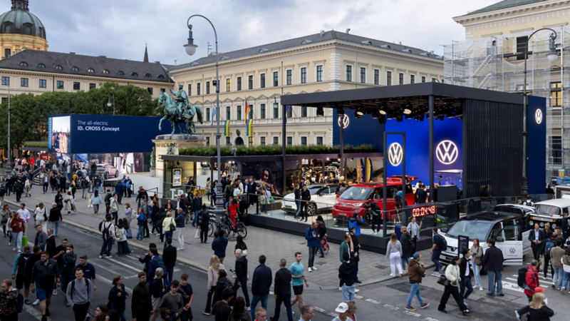 Volkswagen brand pavilion at Odeonsplatz with GTI exhibition area, large LED screen, and many visitors.