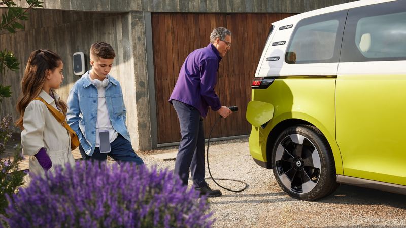 Padre ricarica la batteria della Volkswagen ID. Buzz con i due figli sullo sfondo. 