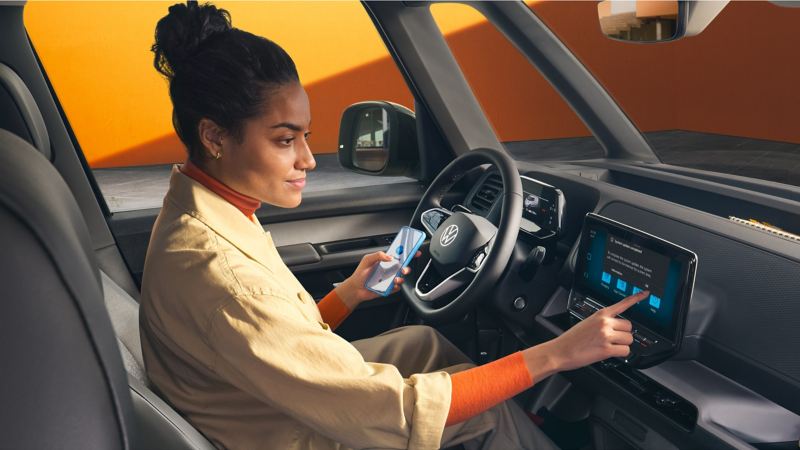 A woman sits in the driver's seat of the ID. Buzz Cargo and connects her mobile phone to the vehicle.