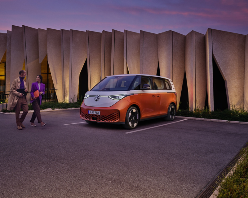 VW ID. Buzz orange garé avec un homme et une femme qui marchent