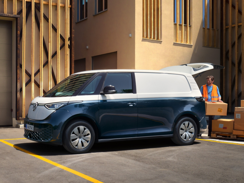 Un VW ID. Buzz Cargo bleu et blanc devant un hangar se faisant charger par 1 personne