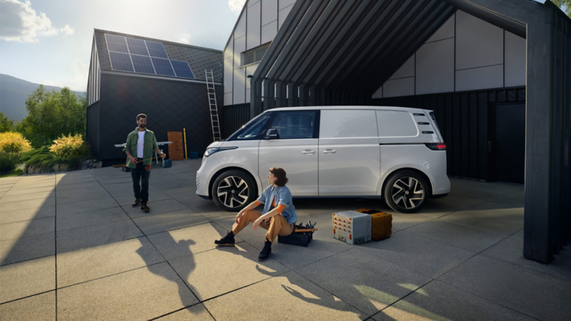Två sollcellsinstallatörer tar en paus bredvid en vit VW ID. Buzz Cargo elskåpbil