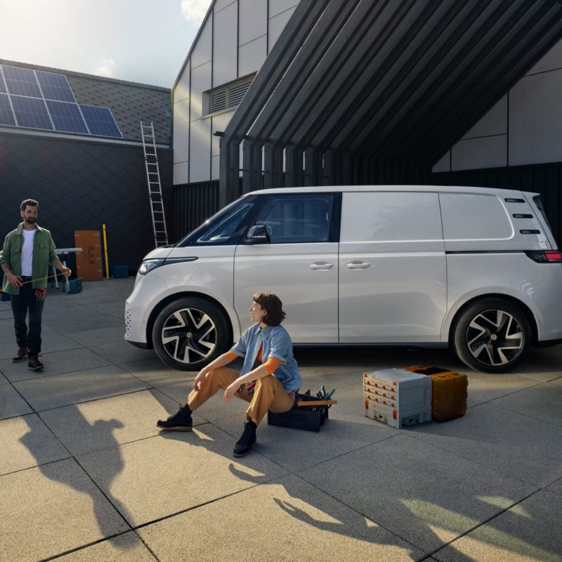 Två sollcellsinstallatörer tar en paus bredvid en vit VW ID. Buzz Cargo elskåpbil