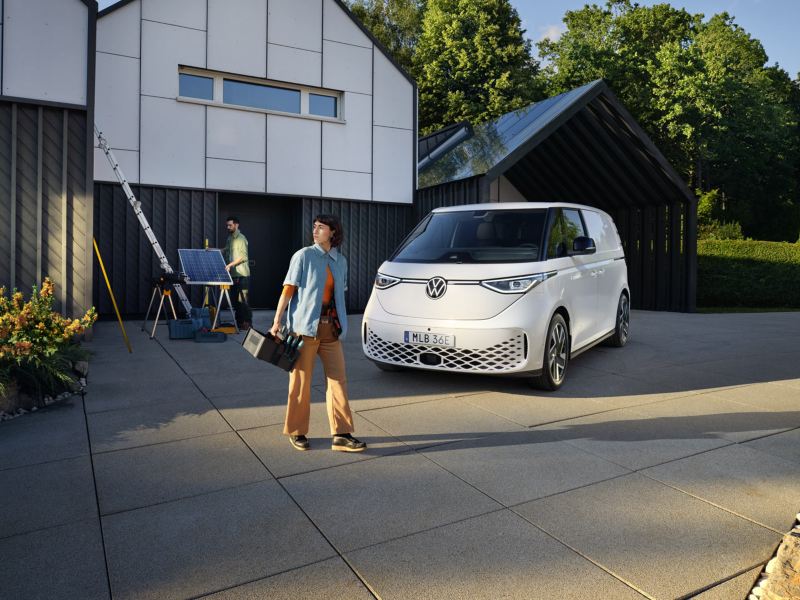 Vit VW ID Buzz Cargo parkerad framför ett hus där två personer installerar solceller