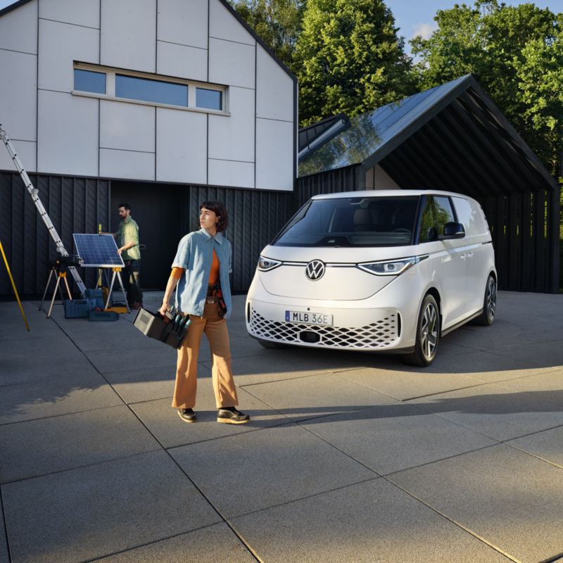 Vit VW ID Buzz Cargo parkerad framför ett hus där två personer installerar solceller