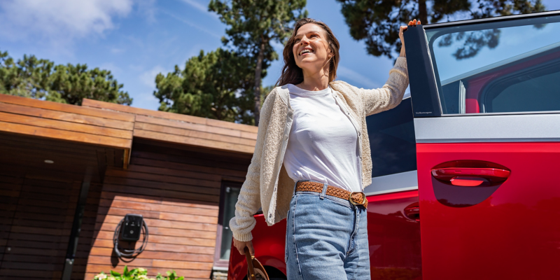 Eine Frau öffnet die Beifahrertür eines geparkten VW ID. Buzz.