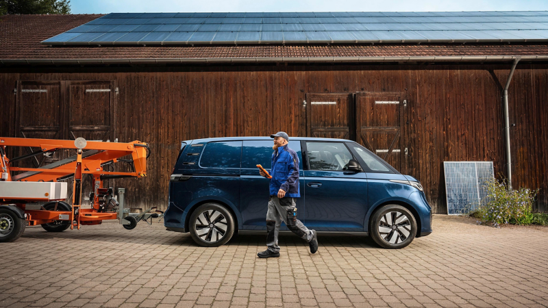 En man går bredvid en VW ID. Buzz Cargo som har en skylift på dragkroken