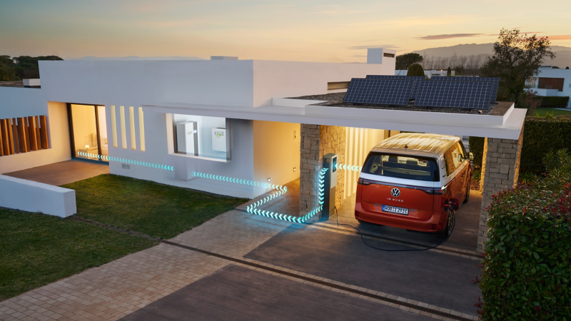 Ein VW ID. Buzz steht unter dem Carport eines modernen Hauses und wird aufgeladen.