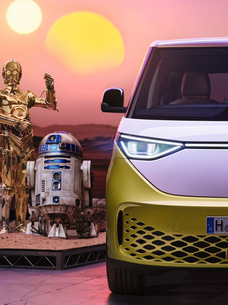Εμπρός όψη ενός λευκού-κίτρινου VW ID. Buzz που φαίνεται να παρκάρει σε έναν άγνωστο πλανήτη και φορτίζει με ρεύμα. 2 Droids του Star Wars βρίσκονται δίπλα του. 