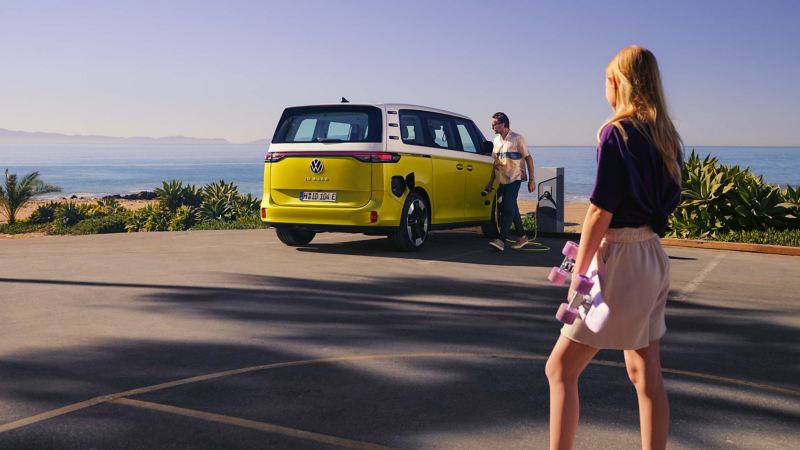 A man plugging an ID. Buzz into a charging station parked next to a beach.