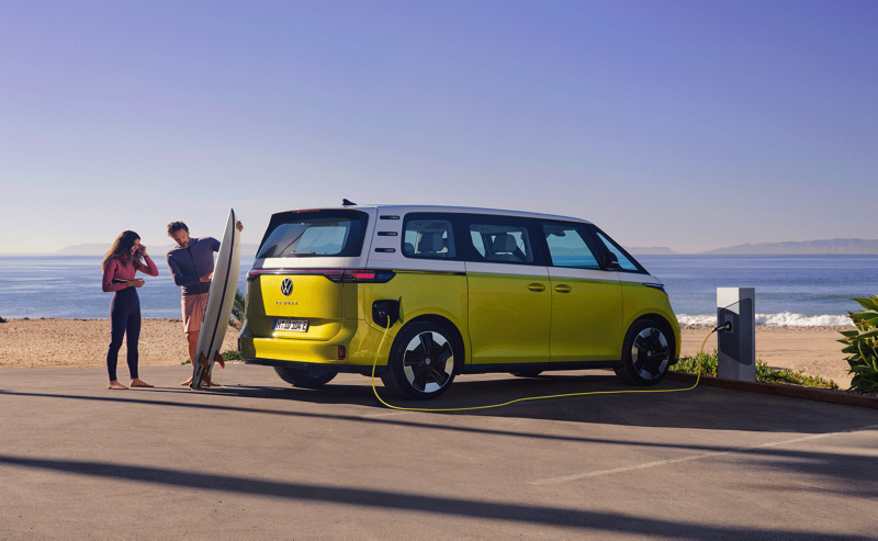 VW ID. Buzz stoi przy plaży, przed samochodem mężczyzna pokazuje córce deskę surfingową.