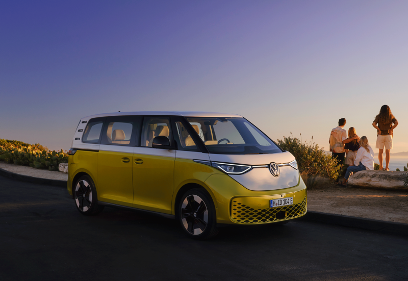 Un Volkswagen ID. Buzz jaune et blanc stationné sur le bord de la route avec une famille qui regarde vers la mer