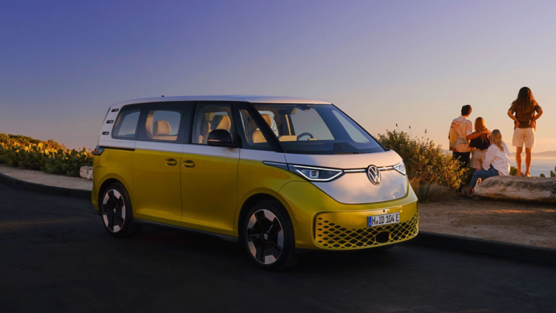 Un Volkswagen ID. Buzz jaune et blanc stationné sur le bord de la route avec une famille qui regarde vers la mer.