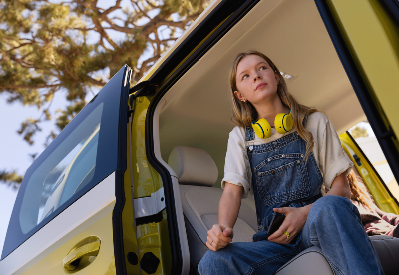 A girl with yellow headphones sits in the side door of the VW ID. Buzz.