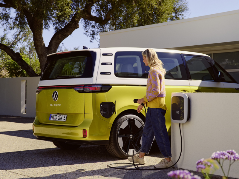 Kvinna som ska sätta i laddaren i en gul-vit VW ID Buzz elbil minibuss