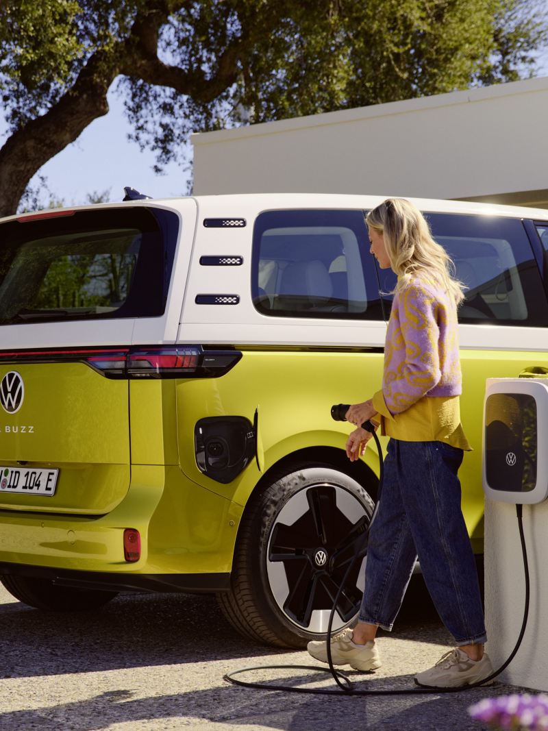 Kvinna som ska sätta i laddaren i en gul-vit VW ID Buzz elbil minibuss