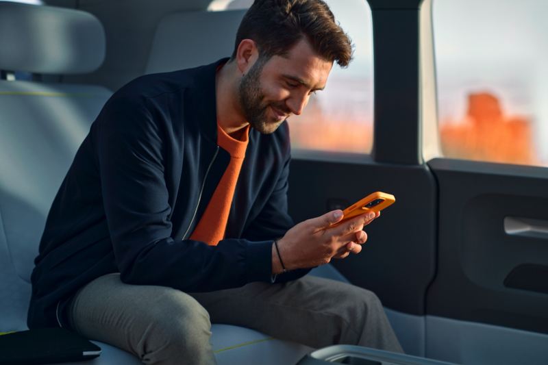 Un homme sur le siège arrière du Volkswagen ID. Buzz, le regard rivé sur son smartphone.