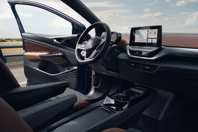 Interior view of the cockpit in the VW ID.4 with multifunction steering wheel, center console and touch display. View from the windshield of the blue sky with the door open.