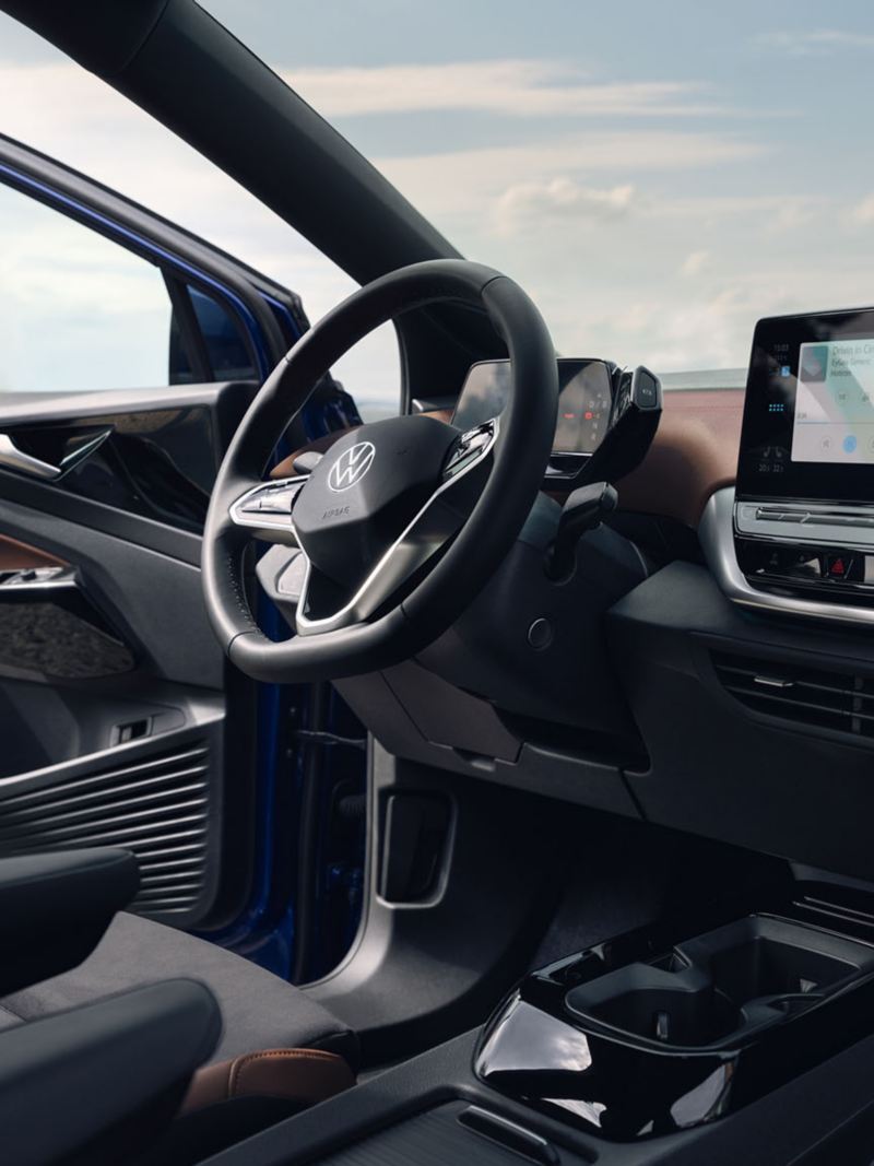 Binnenaanzicht van de cockpit van een VW ID.4 met multifunctioneel stuur, middenconsole en touchscreen. Zicht op de voorruit op de blauwe hemel; de deur is geopend.
