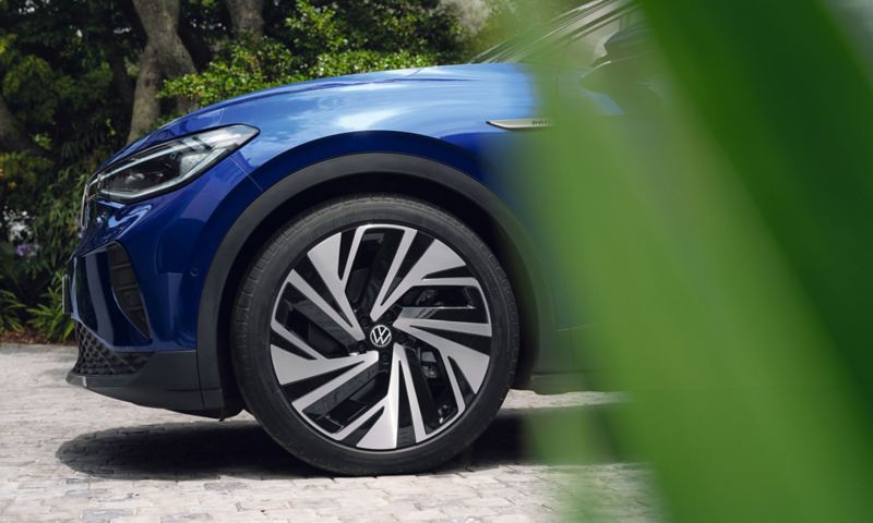 Vue frontale latérale d’une VW ID.4 bleue en stationnement. Gros plan d’un pneu avant.