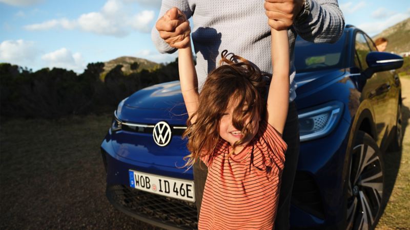 Ένας πατέρας σηκώνει ένα κοριτσάκι ψηλά κρατώντας το από τα χέρια και εκείνο είναι χαρούμενο μπροστά από ένα ID.4