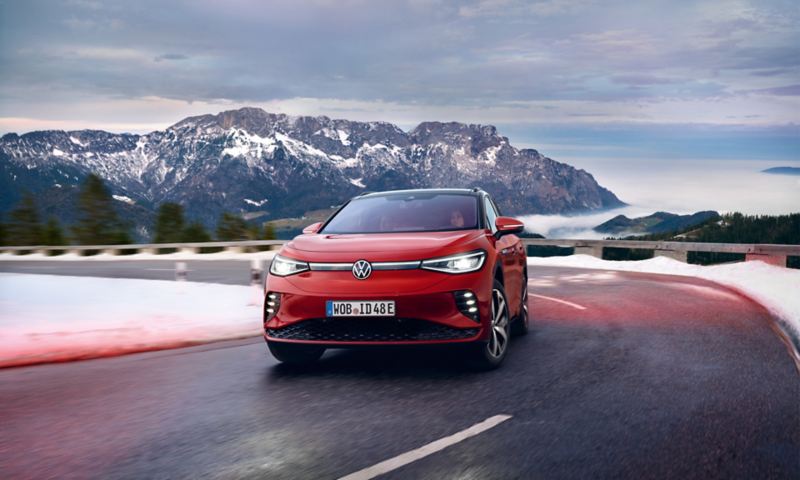 VW ID.4 GTX in red from the front. Drives on country road in front of snow-capped mountains