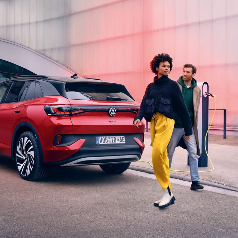 Punainen VW ID.4 GTX takaa katsottuna, kaksi henkilöä ylittää tietä