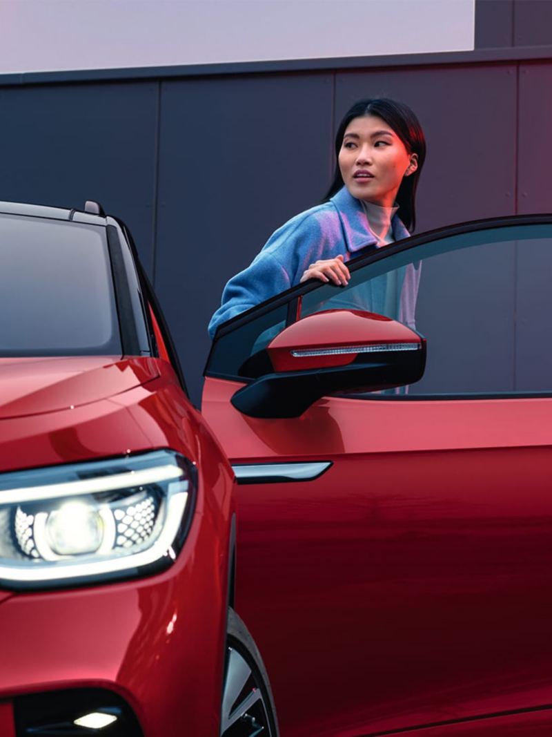 Punainen VW ID.5 GTX, keula näkyvissä, nainen nousee autosta