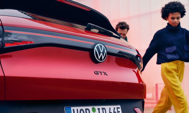 Kobieta i mężczyzna przechodzą obok tylnej klapy czerwonego VW ID.4 GTX