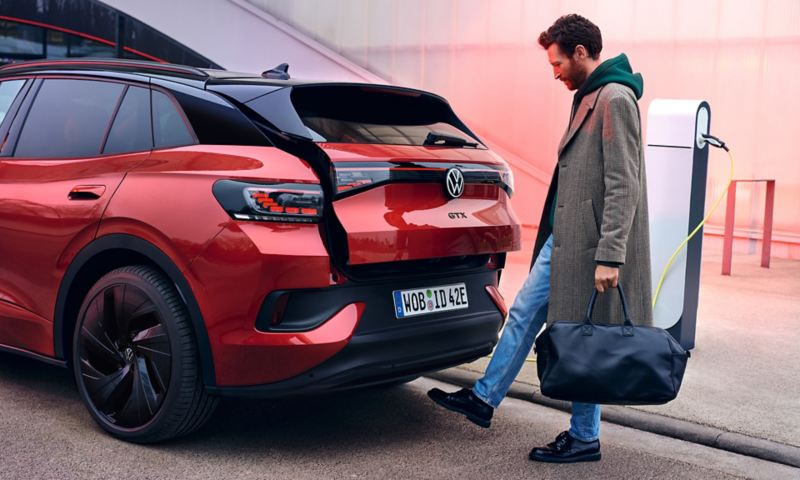 VW ID.4 GTX in Rot von hinten zu sehen, Mann mit Tasche öffnet Heckklappe
