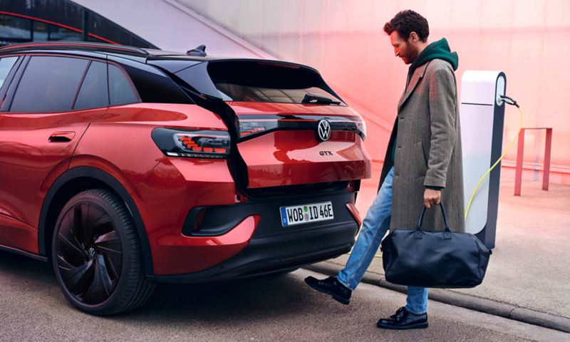 VW ID.4 GTX rouge, vue de l'arrière, un homme portant des sacs ouvre le coffre grâce à la fonctionnalité Easy Open & Close.