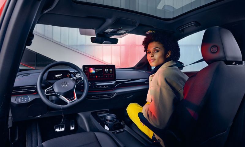 VW ID.4 GTX interior with view of front seats and cockpit. Woman sitting on passenger seat with view to the rear.